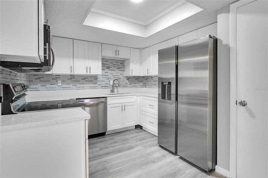 A kitchen features white cabinets, stainless steel appliances, a tiled backsplash, and light wood flooring — 513 FAIRWAYS LANE UNIT B, OCALA, FL