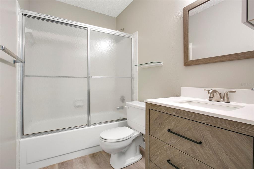 A bathroom features a wood-toned vanity, a white toilet, and a shower-tub with sliding doors — 513 FAIRWAYS LANE UNIT B, OCALA, FL