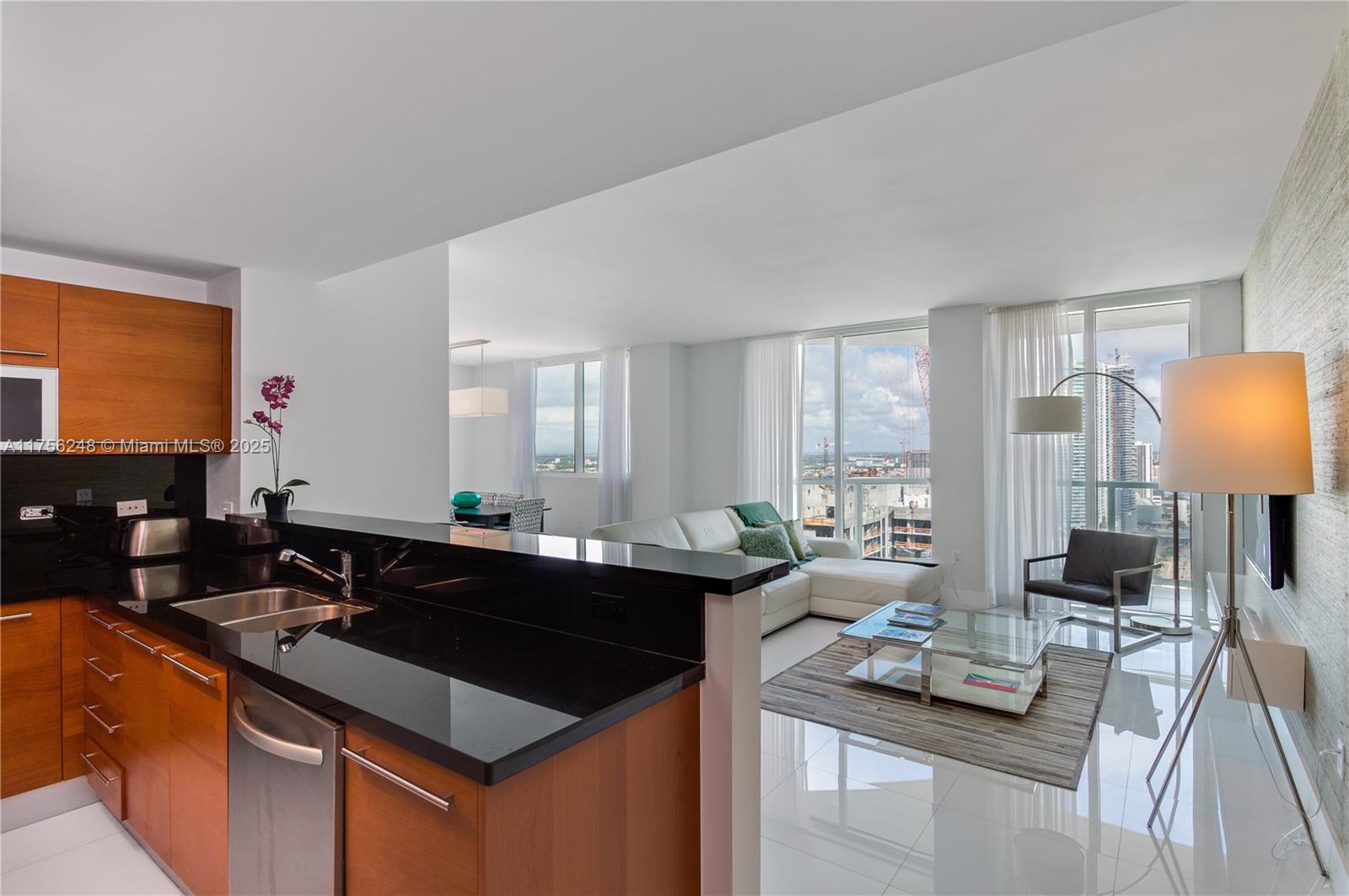 A modern kitchen with black countertops overlooks a living room with floor-to-ceiling windows — 253 NE 2nd St # 3702, Miami FL 33132, MIAMI, FL