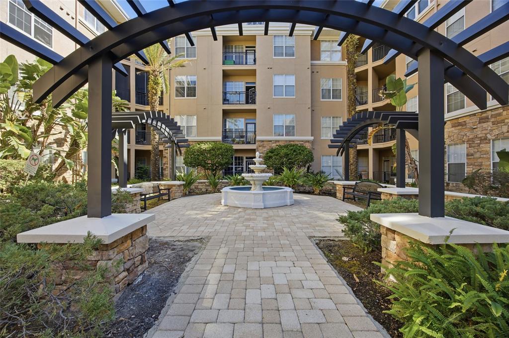 A stone-paved courtyard features a tiered fountain, benches, and a black metal pergola — 4221 W SPRUCE STREET UNIT 2328, TAMPA, FL