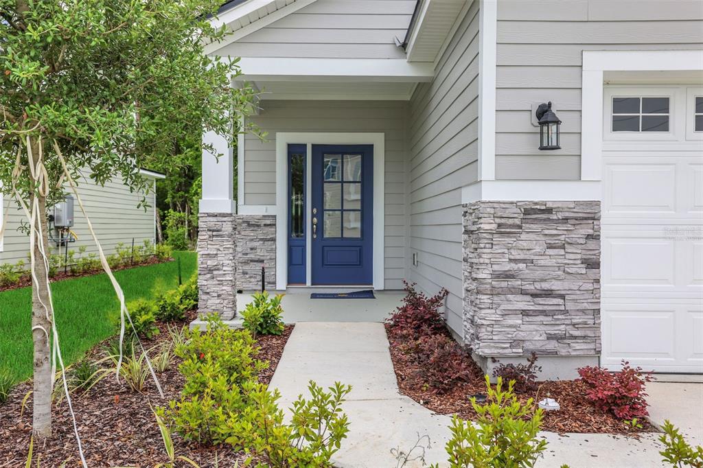 A blue front door with a sidelight is framed by stone accents and gray siding — 674 FARMFIELD DRIVE, ST AUGUSTINE, FL