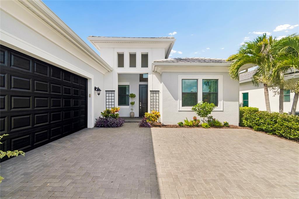 A modern one-story house with a black garage door and a paved driveway — 9005 BERNINI PLACE, SARASOTA, FL