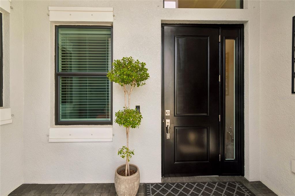 A black front door with a side window and a potted topiary on a porch — 9005 BERNINI PLACE, SARASOTA, FL