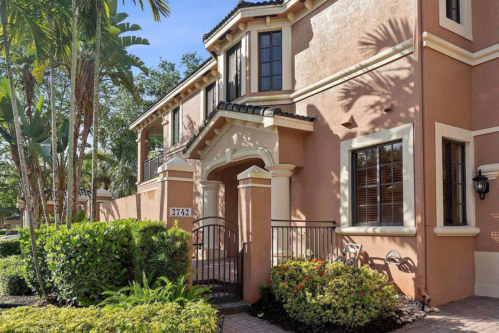 The exterior of a two-story stucco house features a gated courtyard entrance and landscaping — 2742 Kinsington Circle, Weston FL 33332, WESTON, FL