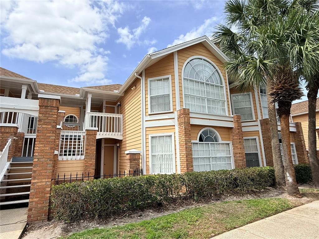 A two-story tan building with brick pillars, white trim, and a palm tree in front — 2490 SWEETWATER CLUB CIRCLE UNIT 67, KISSIMMEE, FL