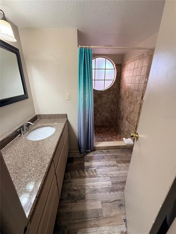 A bathroom features a vanity with a granite countertop, wood-look flooring, and a tiled shower — 2490 SWEETWATER CLUB CIRCLE UNIT 67, KISSIMMEE, FL