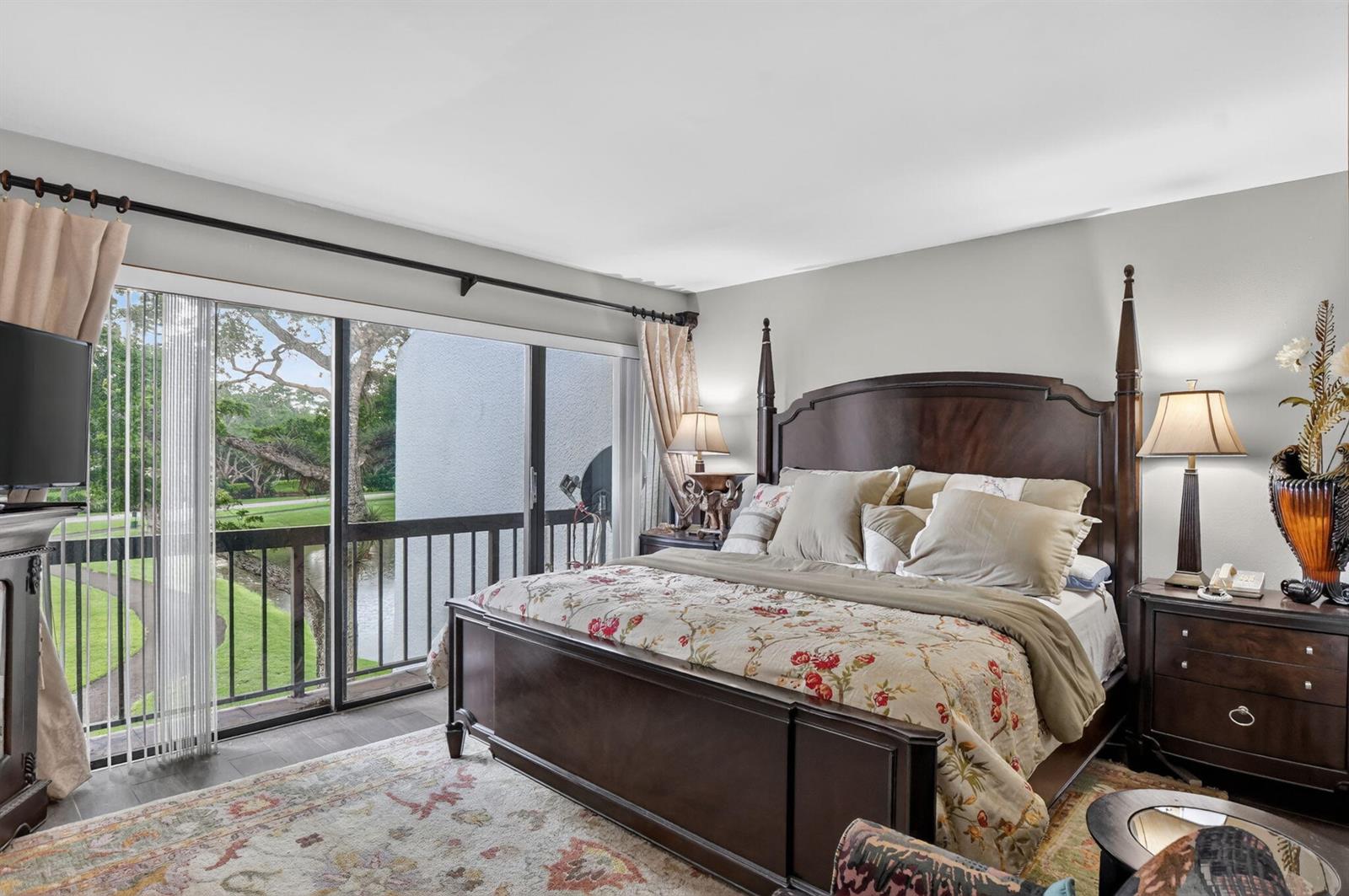 A bedroom features a dark wood four-poster bed, floral bedding, and sliding glass doors overlooking a pond — 2805 Bridgewood Drive, Boca Raton FL 33434, BOCA RATON, FL