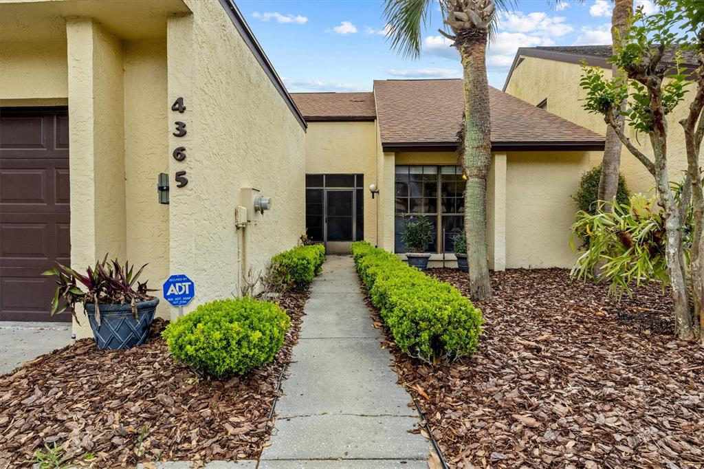 A concrete walkway leads to the front entrance of a tan house with brown trim — 4365 CREEKWOOD LANE UNIT 4365, MULBERRY, FL