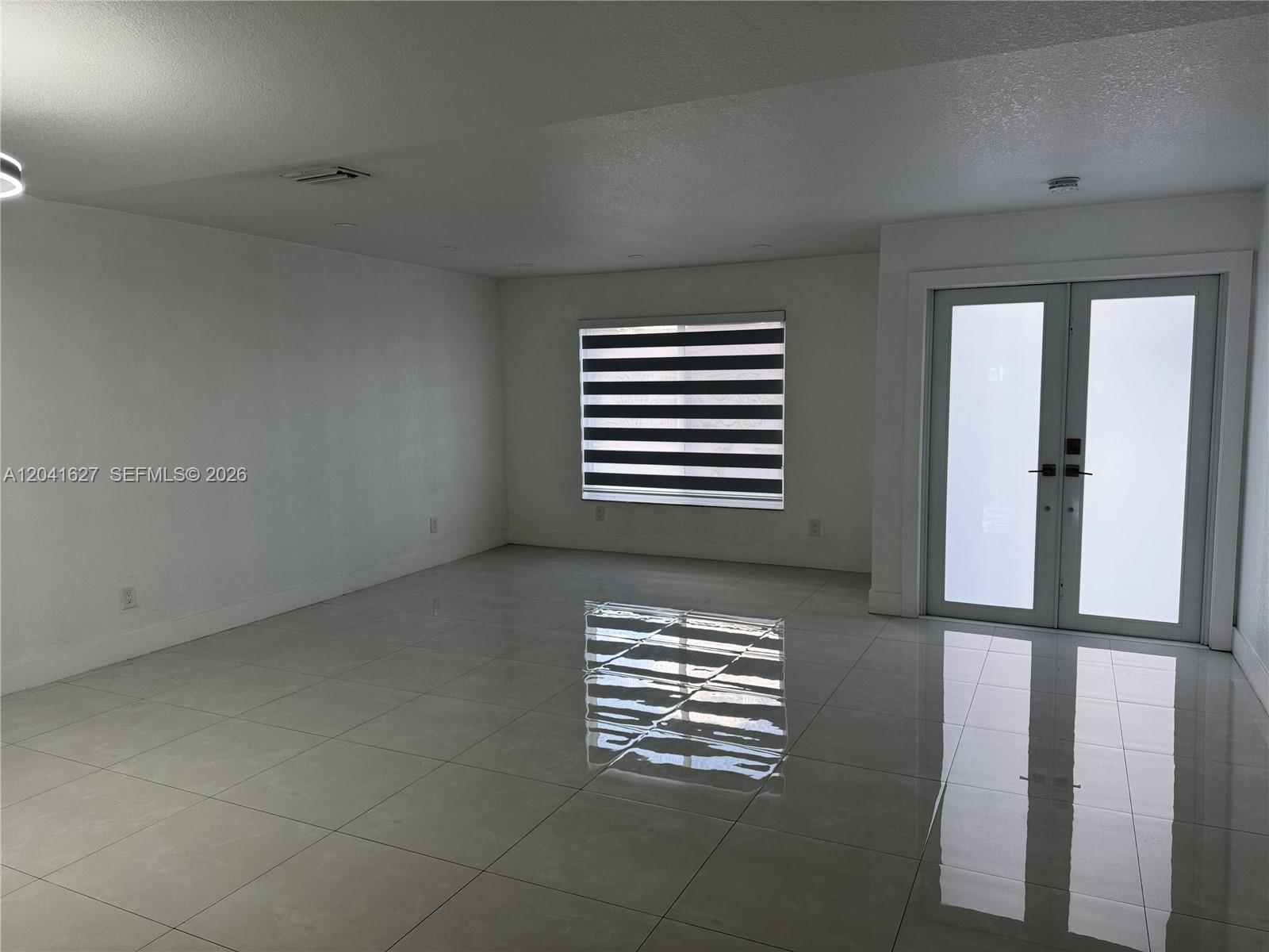 A bright, empty room features white walls, large glossy floor tiles, and a glass-paned door — 2401 SW 143rd Ct, Miami FL 33175, MIAMI, FL