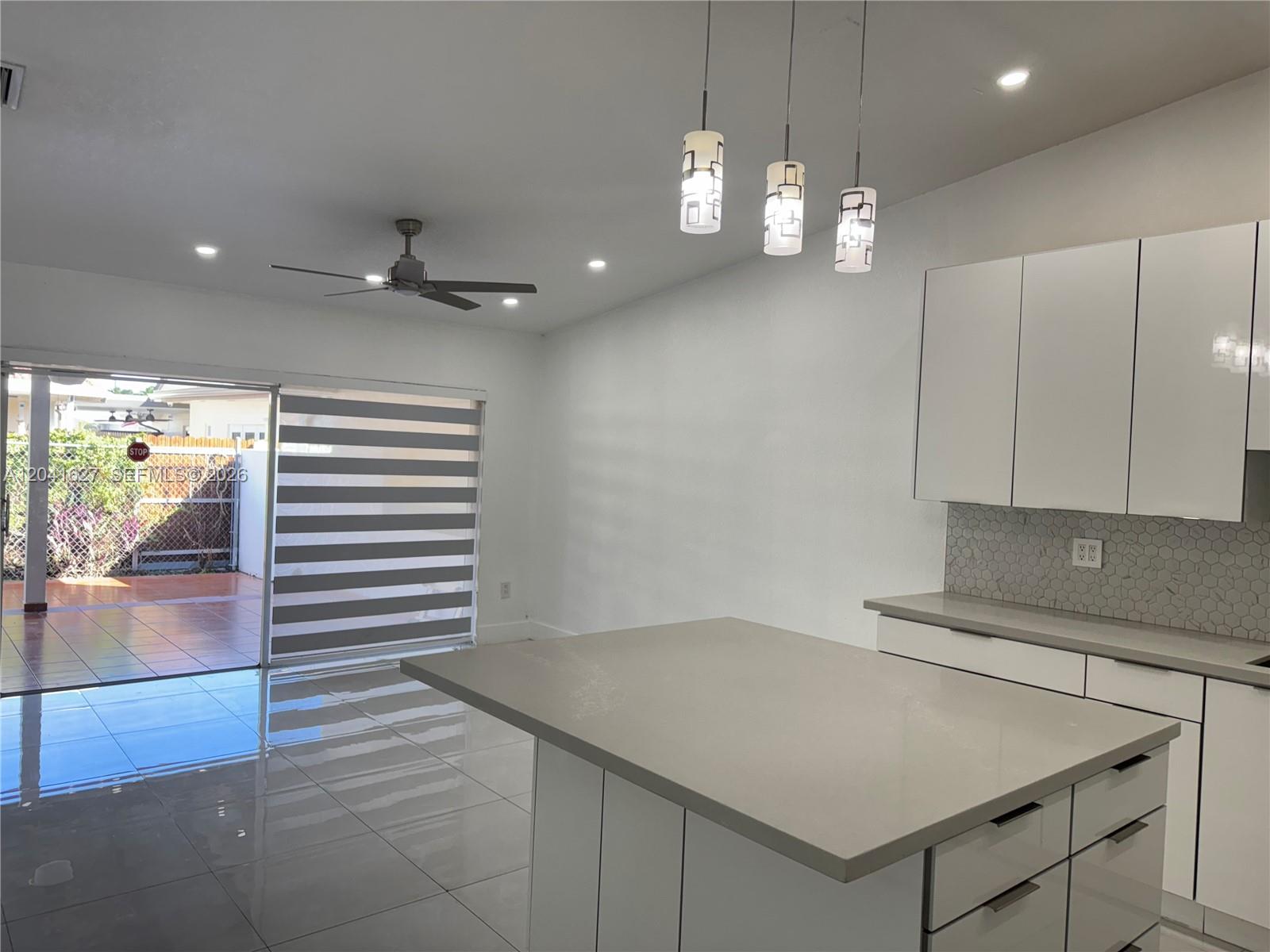 A modern kitchen with a large island, white cabinets, and a sliding door to a patio — 2401 SW 143rd Ct, Miami FL 33175, MIAMI, FL