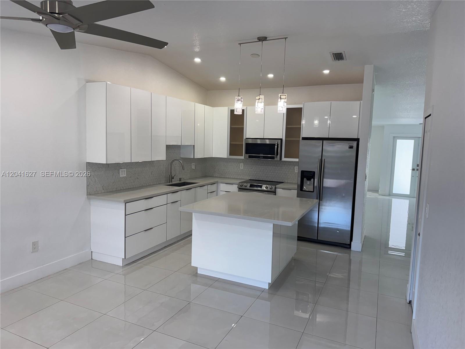 A modern kitchen features white cabinets, stainless steel appliances, a center island, and tiled flooring — 2401 SW 143rd Ct, Miami FL 33175, MIAMI, FL