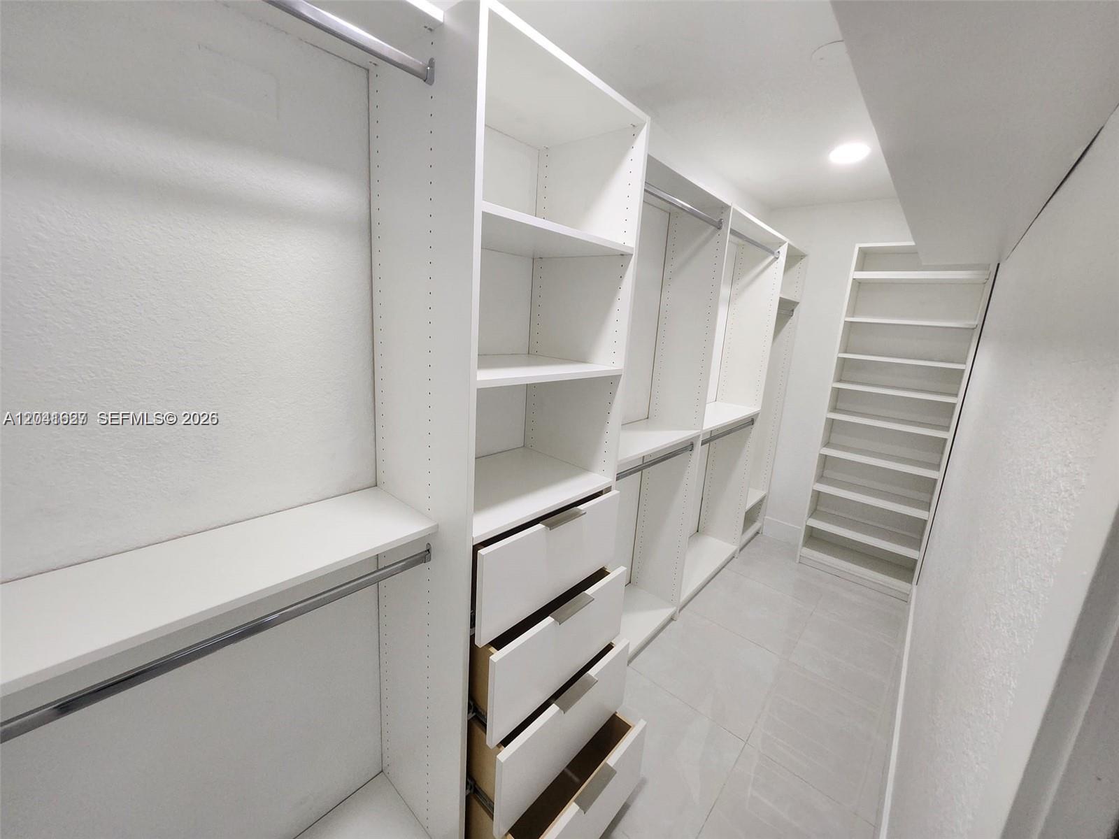 A walk-in closet features white shelving, hanging rods, and drawers on a tiled floor — 2401 SW 143rd Ct, Miami FL 33175, MIAMI, FL
