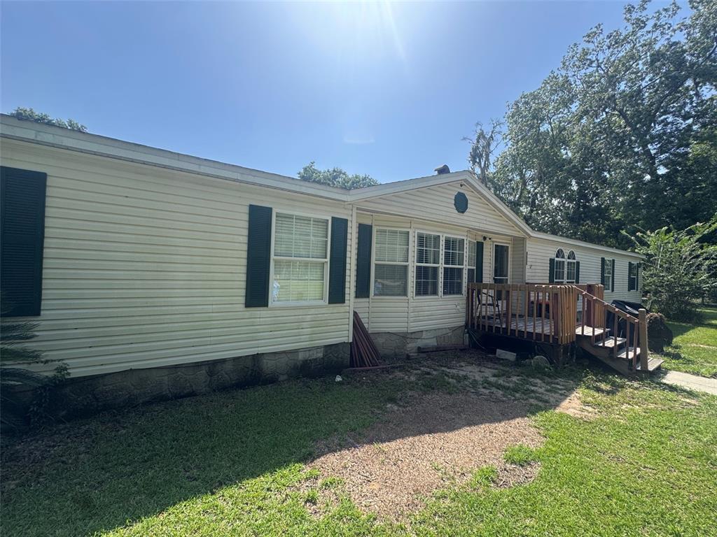 A single-story manufactured home with light siding, dark shutters, and a wooden deck — 4650 SW 36 STREET, OCALA, FL