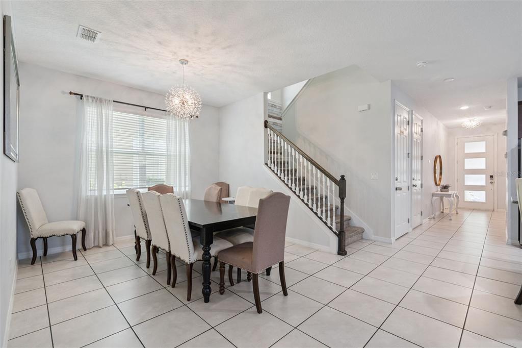 A dining room with a dark wood table, upholstered chairs, tile flooring, and a staircase — 1633 NASSAU POINT TRAIL, KISSIMMEE, FL