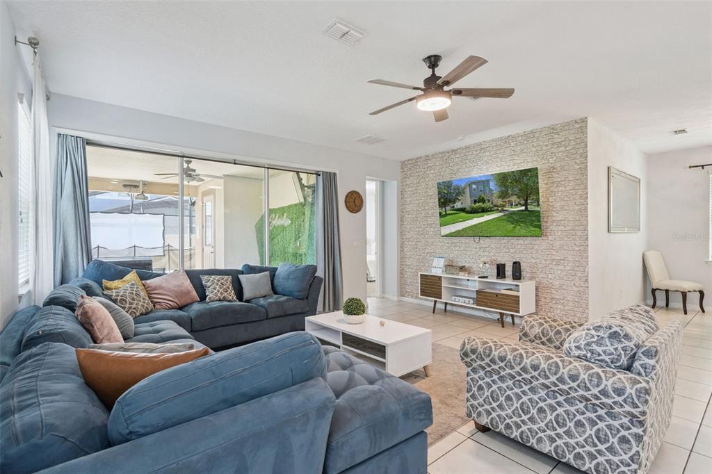 A living room features a blue sectional sofa, a patterned armchair, and a stone-accented wall — 1633 NASSAU POINT TRAIL, KISSIMMEE, FL