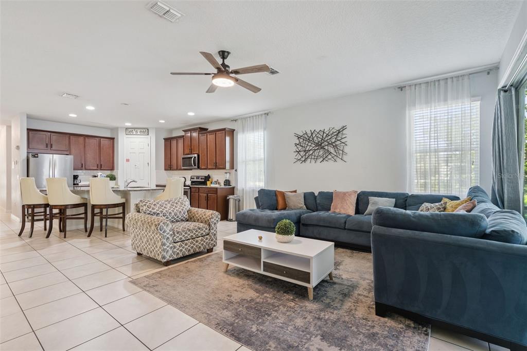 An open-concept living room and kitchen featuring dark wood cabinets, tile flooring, and blue furniture — 1633 NASSAU POINT TRAIL, KISSIMMEE, FL