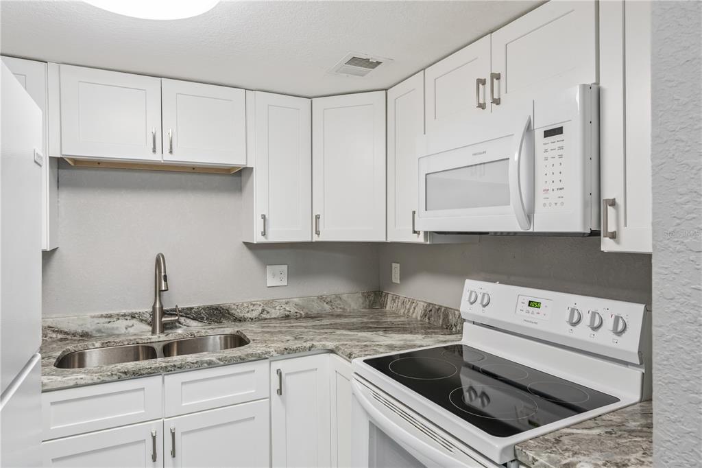 A kitchen features white cabinets, granite countertops, a double sink, and white appliances — 950 LAKE DESTINY ROAD UNIT B, ALTAMONTE SPRINGS, FL