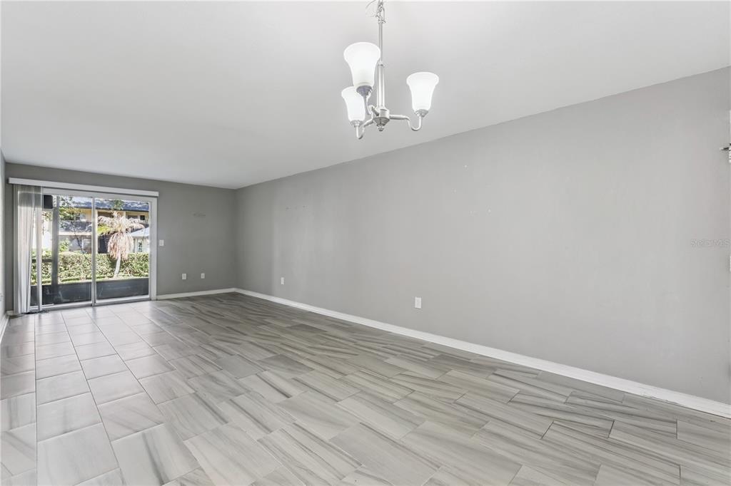 An empty living room features gray tile flooring, light gray walls, and a glass sliding door — 950 LAKE DESTINY ROAD UNIT B, ALTAMONTE SPRINGS, FL