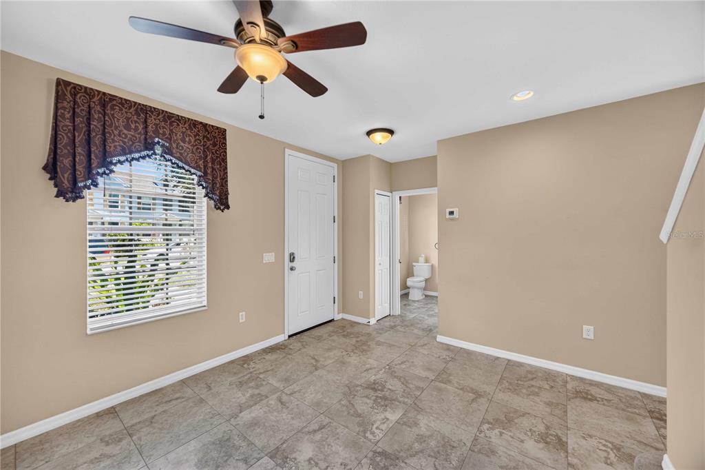 A room with tan walls, tile flooring, a ceiling fan, and a doorway to a bathroom — 5653 WHITEHEAD STREET, BRADENTON, FL