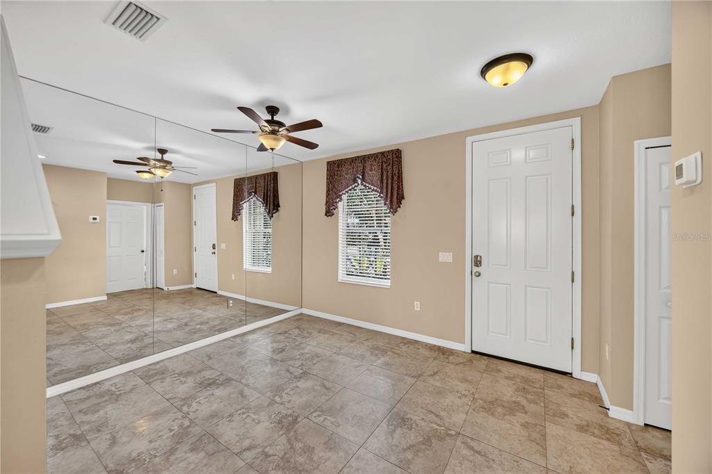 A room with tiled floors, a mirrored wall, a ceiling fan, and a white front door — 5653 WHITEHEAD STREET, BRADENTON, FL