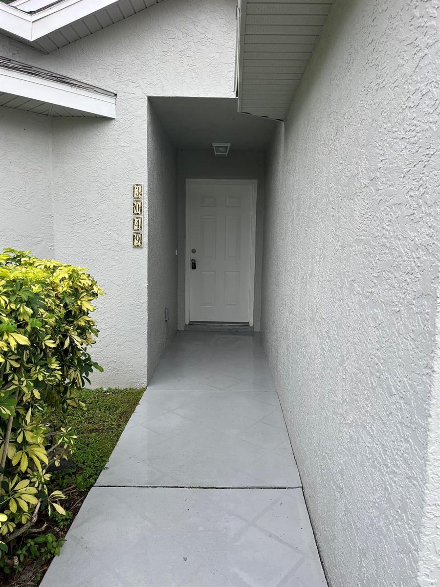 A white front door is recessed in a covered entryway with a gray concrete walkway — 3049 SE 38th Avenue, Okeechobee FL 34974, OKEECHOBEE, FL