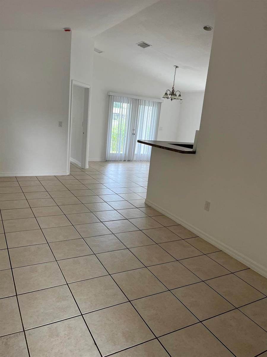 A view of a tiled living area with a breakfast bar and sliding glass doors — 3049 SE 38th Avenue, Okeechobee FL 34974, OKEECHOBEE, FL