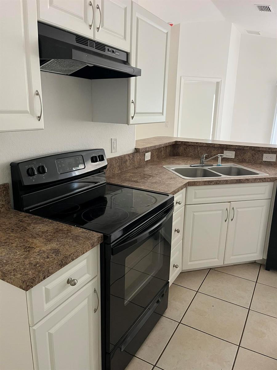 A kitchen features white cabinets, dark countertops, a black stove, and a corner sink — 3049 SE 38th Avenue, Okeechobee FL 34974, OKEECHOBEE, FL