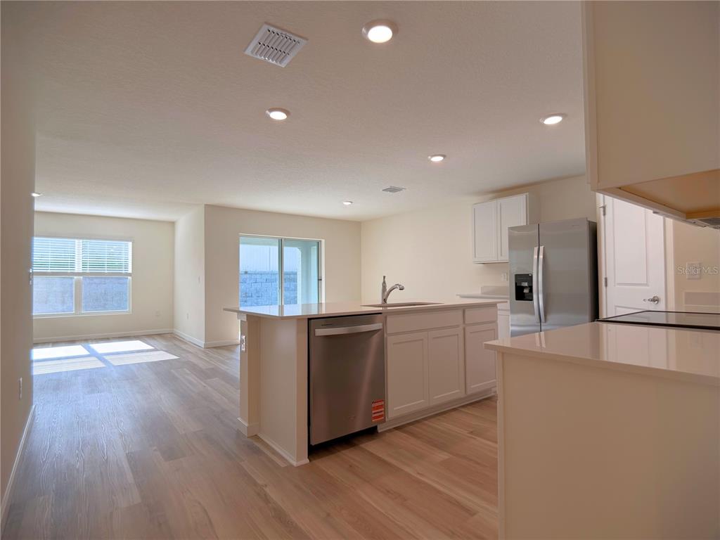 A modern kitchen with white cabinets, stainless steel appliances, and an island overlooks a living area — 11331 SE 72ND COURT, BELLEVIEW, FL