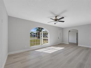 A bright, empty living room features light gray walls, wood-look flooring, and an arched window — 2064 Atlantic Boulevard, Vero Beach FL 32960, VERO BEACH, FL