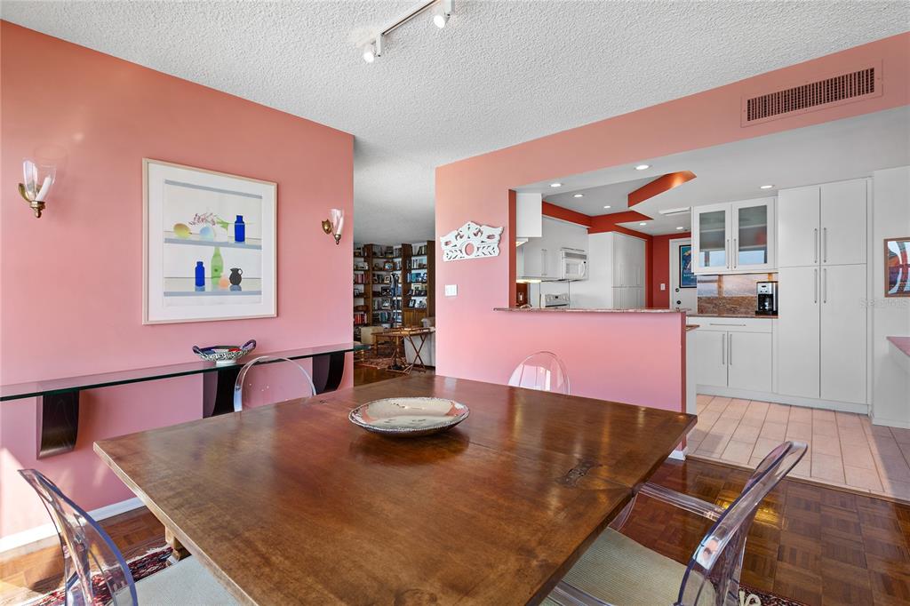 A dining room with a wooden table, clear chairs, and pink walls, opening to a kitchen — 601 LONGBOAT CLUB ROAD UNIT 902S, LONGBOAT KEY, FL