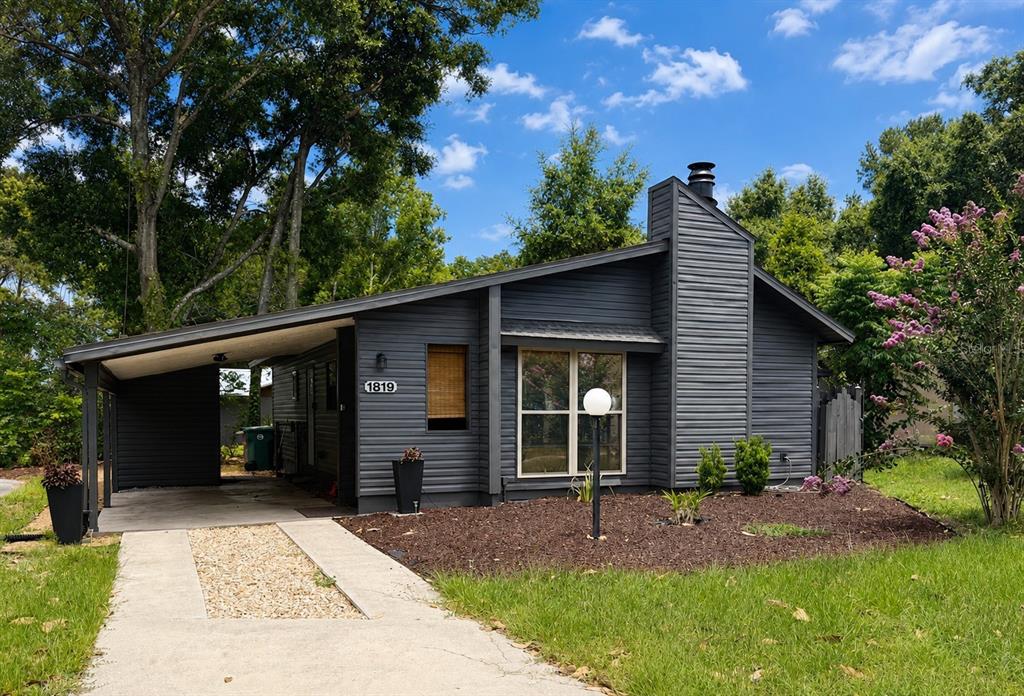 A dark gray single-story house with a carport, chimney, and a gravel-accented concrete driveway — 1819 SW 29TH TERRACE, OCALA, FL