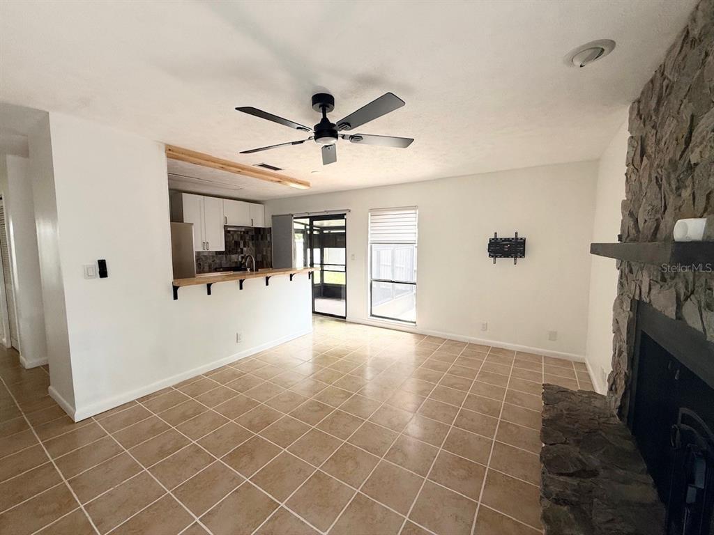 A living room with tile flooring, a stone fireplace, and an open kitchen breakfast bar — 1819 SW 29TH TERRACE, OCALA, FL
