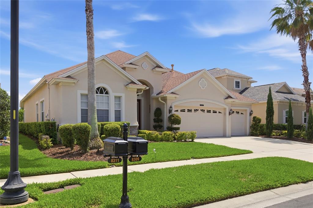 A beige single-story house with a three-car garage and a manicured lawn — 8309 OLD TOWN DRIVE, TAMPA, FL