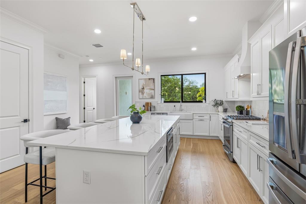 A modern white kitchen features a large marble-topped island, stainless steel appliances, and wood flooring — 4509 W NORTH A STREET UNIT 1, TAMPA, FL
