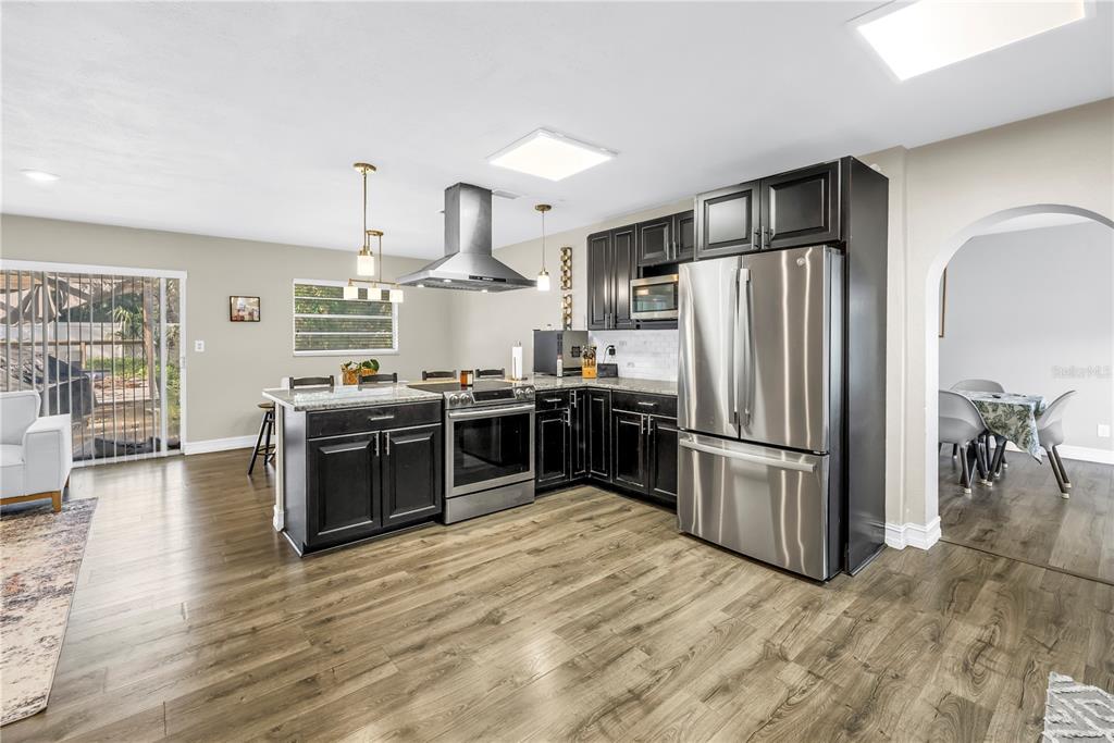 A kitchen with dark cabinets, stainless steel appliances, and wood-look flooring opens to a dining area — 4708 W COACHMAN AVENUE, TAMPA, FL