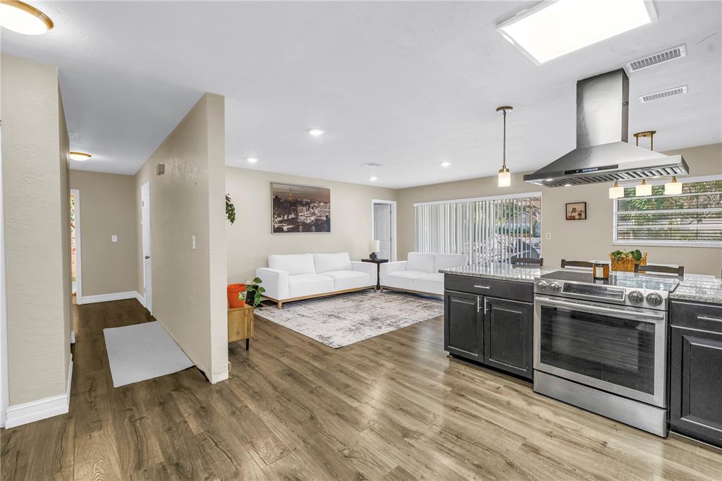 An open-concept kitchen and living area featuring dark cabinets, stainless steel appliances, and wood flooring — 4708 W COACHMAN AVENUE, TAMPA, FL