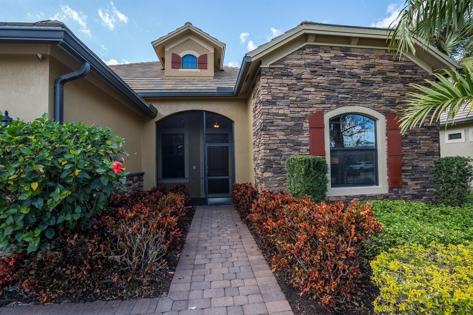 A stone-accented house exterior features a brick walkway leading to a screened-in front entryway — 4127 Siena Circle, Wellington FL 33414, WELLINGTON, FL