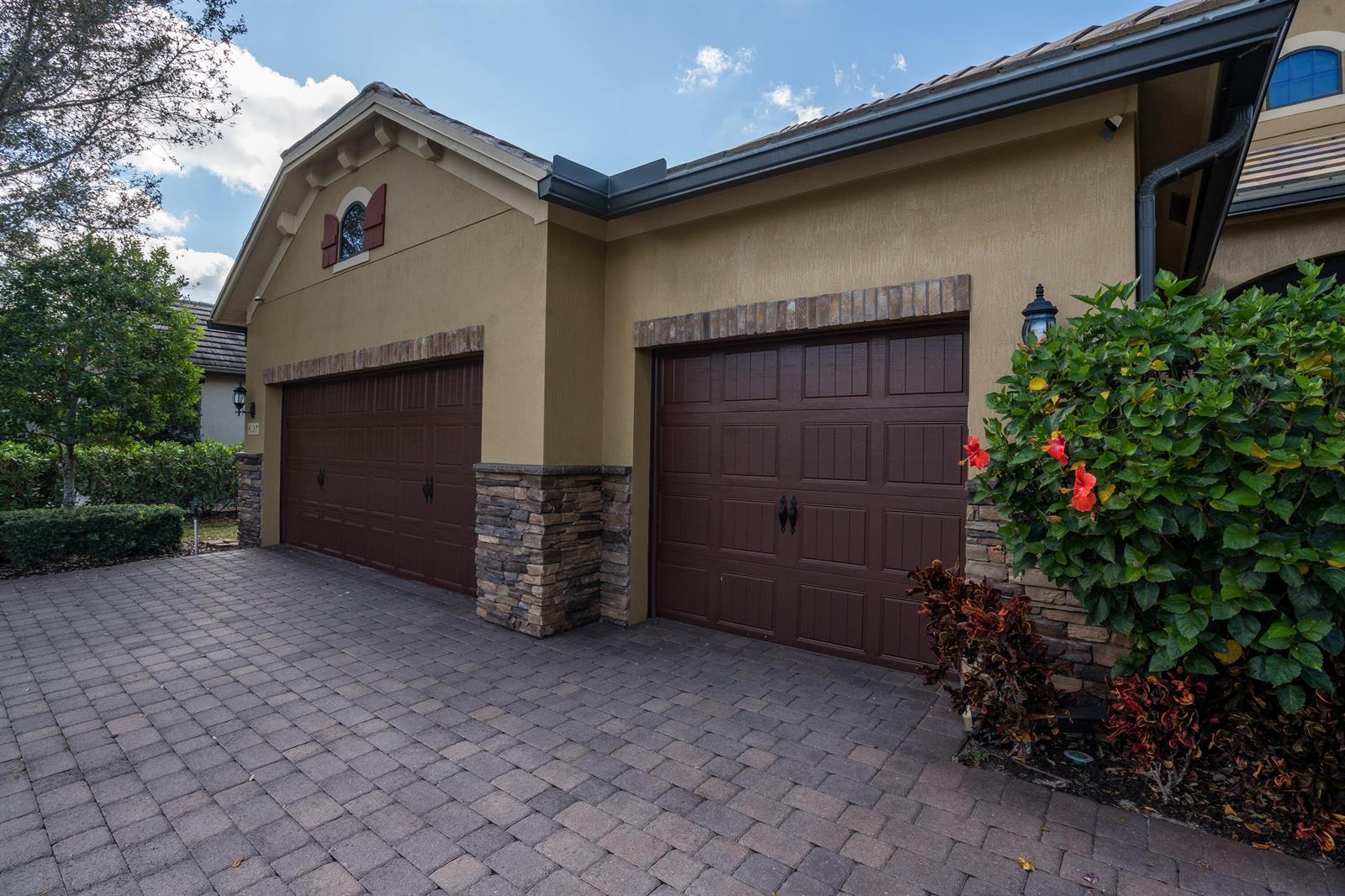 A two-car garage with brown doors, stone accents, and a paved driveway under a blue sky — 4127 Siena Circle, Wellington FL 33414, WELLINGTON, FL