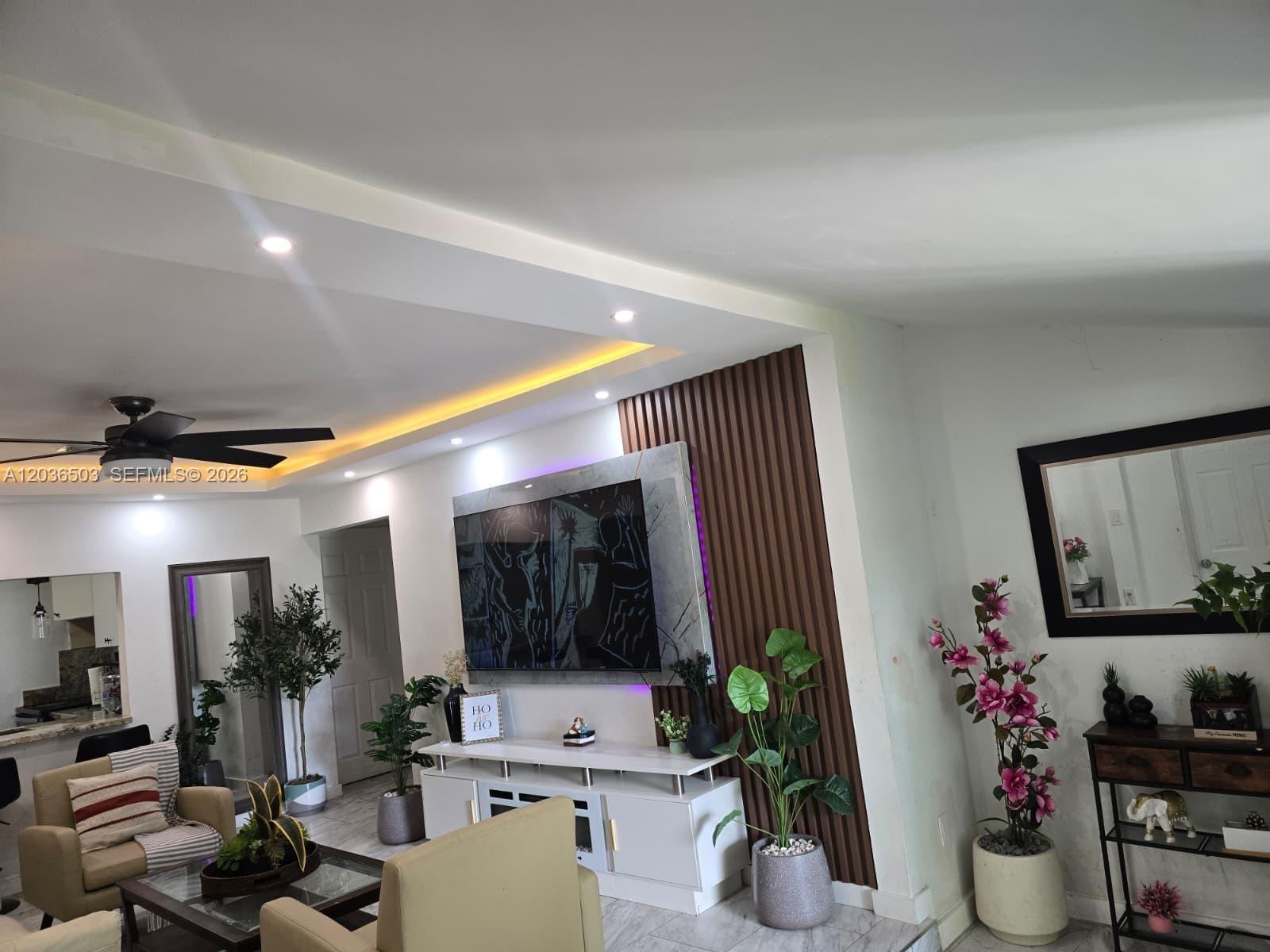 A living room features a wall-mounted television, wood slat paneling, and a white media console — 1055 NW 58th Ter, Miami FL 33127, MIAMI, FL