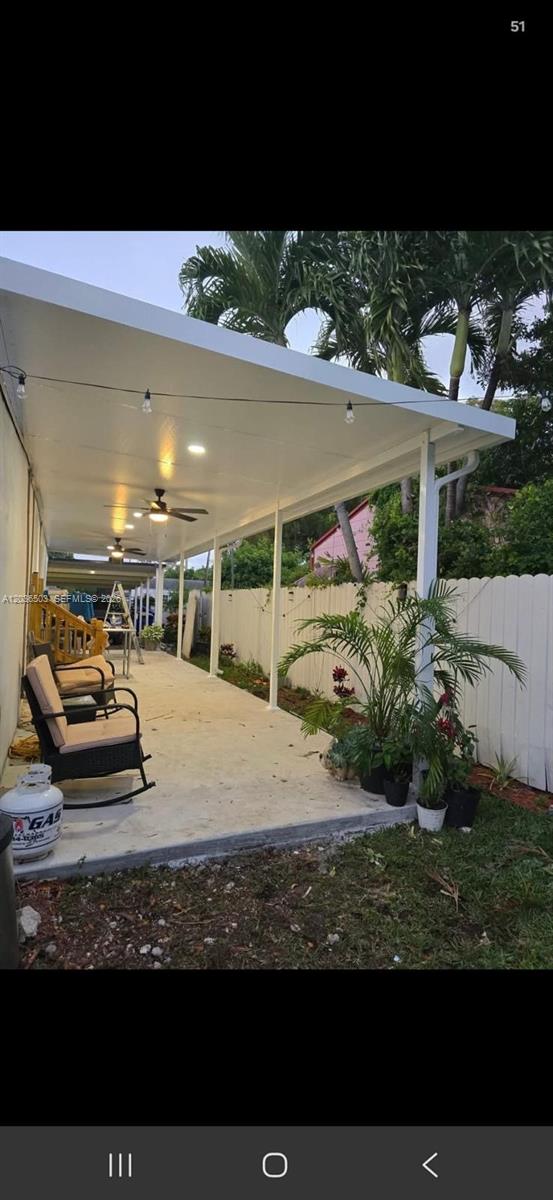 A covered concrete patio features white support columns, ceiling fans, and string lights — 1055 NW 58th Ter, Miami FL 33127, MIAMI, FL
