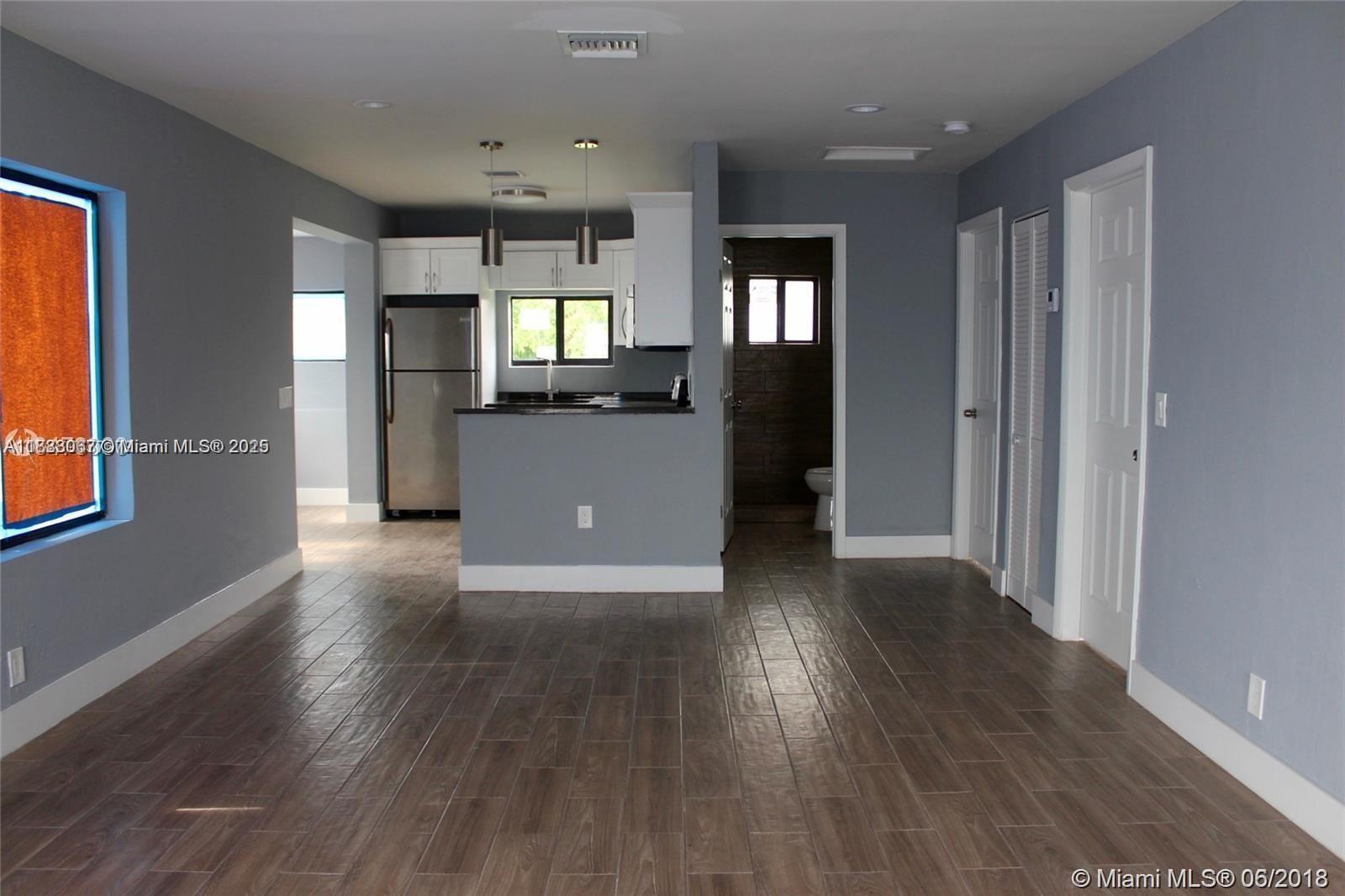 An open-concept living area features gray walls, wood-look tile flooring, and a kitchen with white cabinets — 107 W Pembroke Rd, Hallandale Beach FL 33009, HALLANDALE BEACH, FL