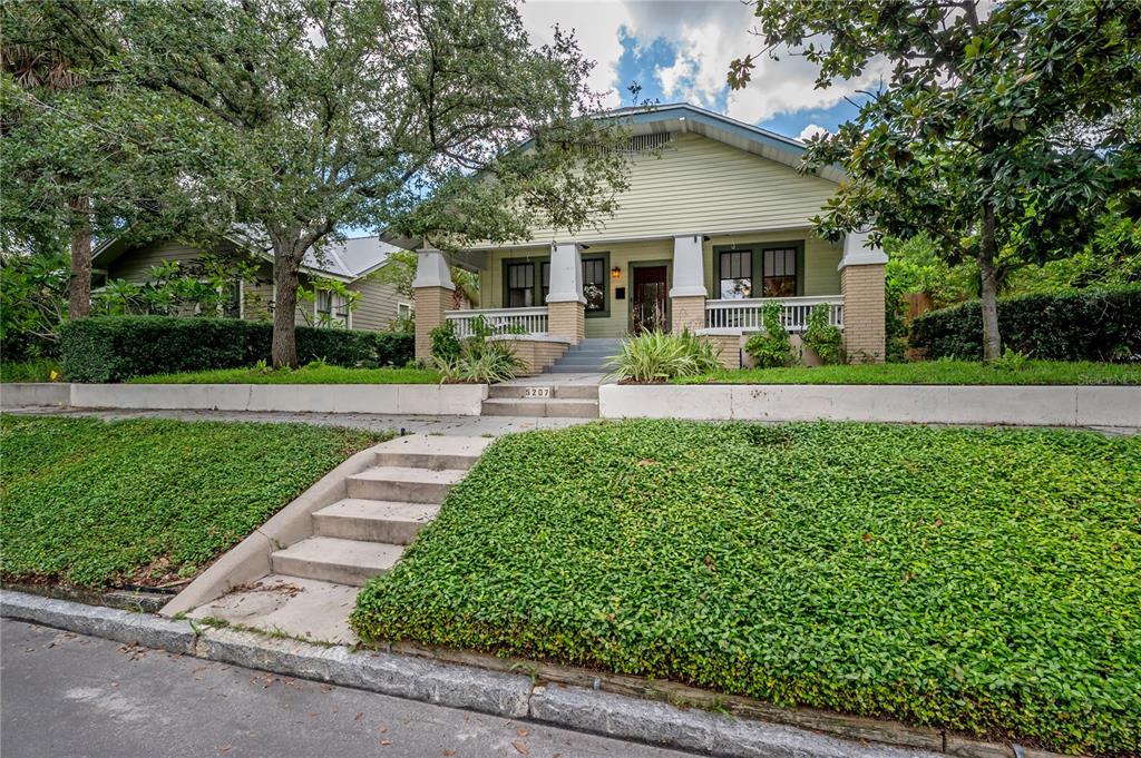 A light green bungalow with a front porch sits behind a terraced, landscaped yard — 5207 N SUWANEE AVENUE, TAMPA, FL
