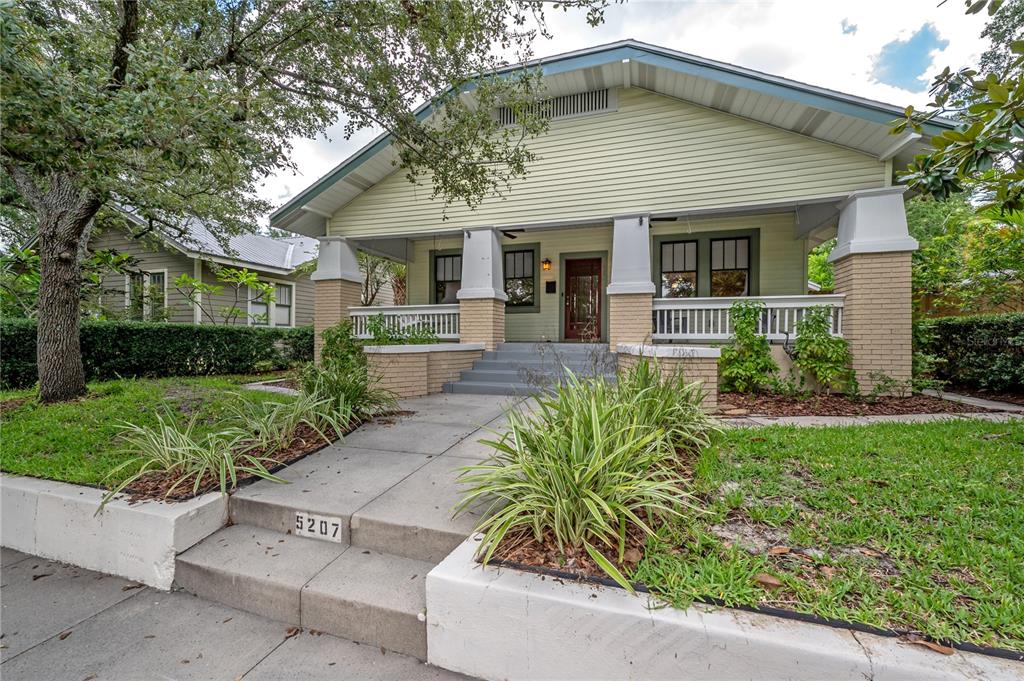 A light green bungalow with a front porch, brick pillars, and a concrete walkway — 5207 N SUWANEE AVENUE, TAMPA, FL