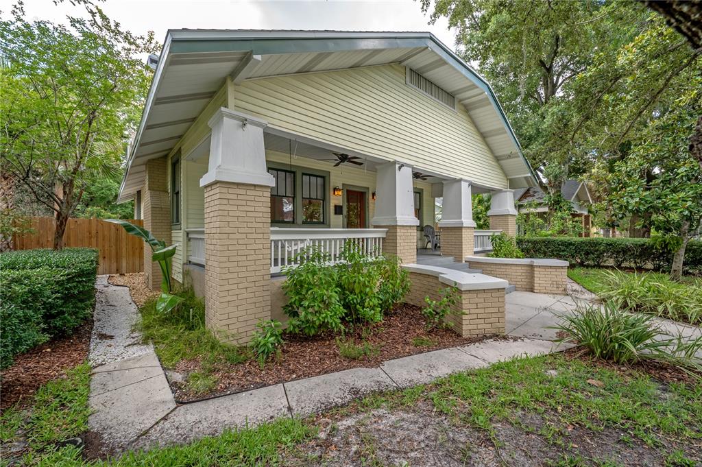 A yellow bungalow with a brick-based front porch and white columns sits in a yard — 5207 N SUWANEE AVENUE, TAMPA, FL