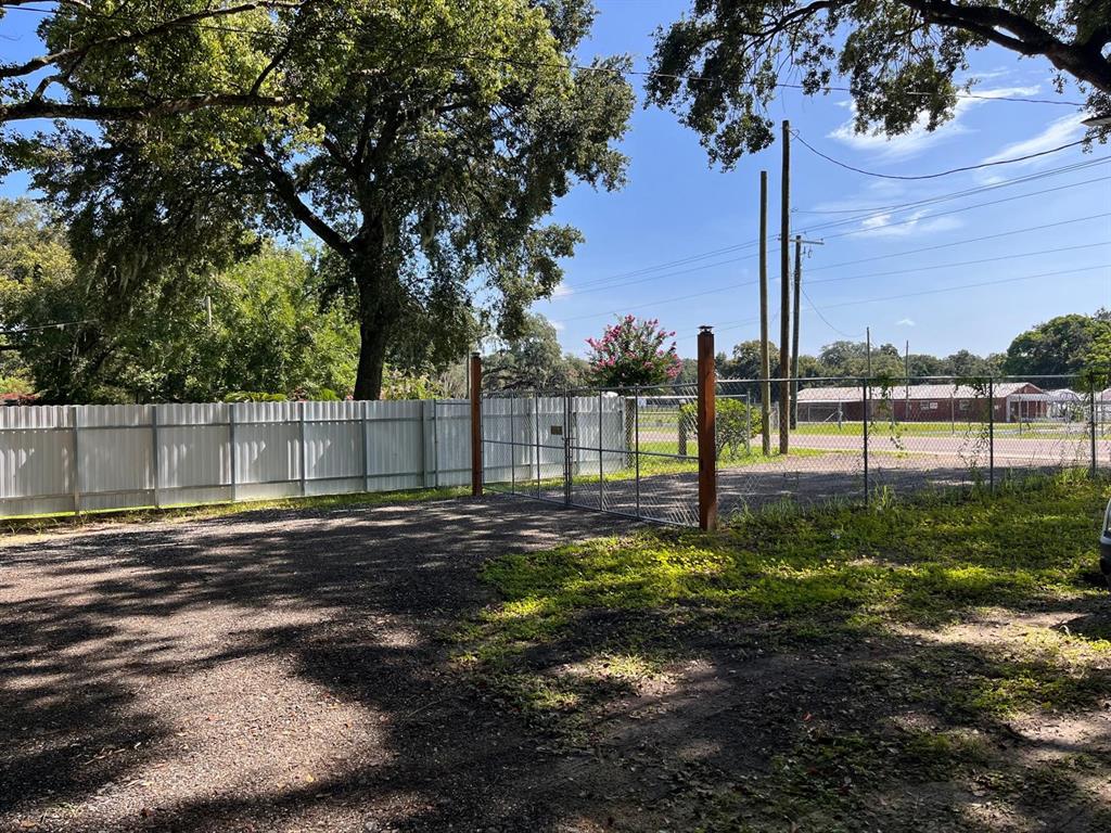 A gravel driveway leads to a chain-link gate and a white metal privacy fence — 10516 579 HIGHWAY, THONOTOSASSA, FL
