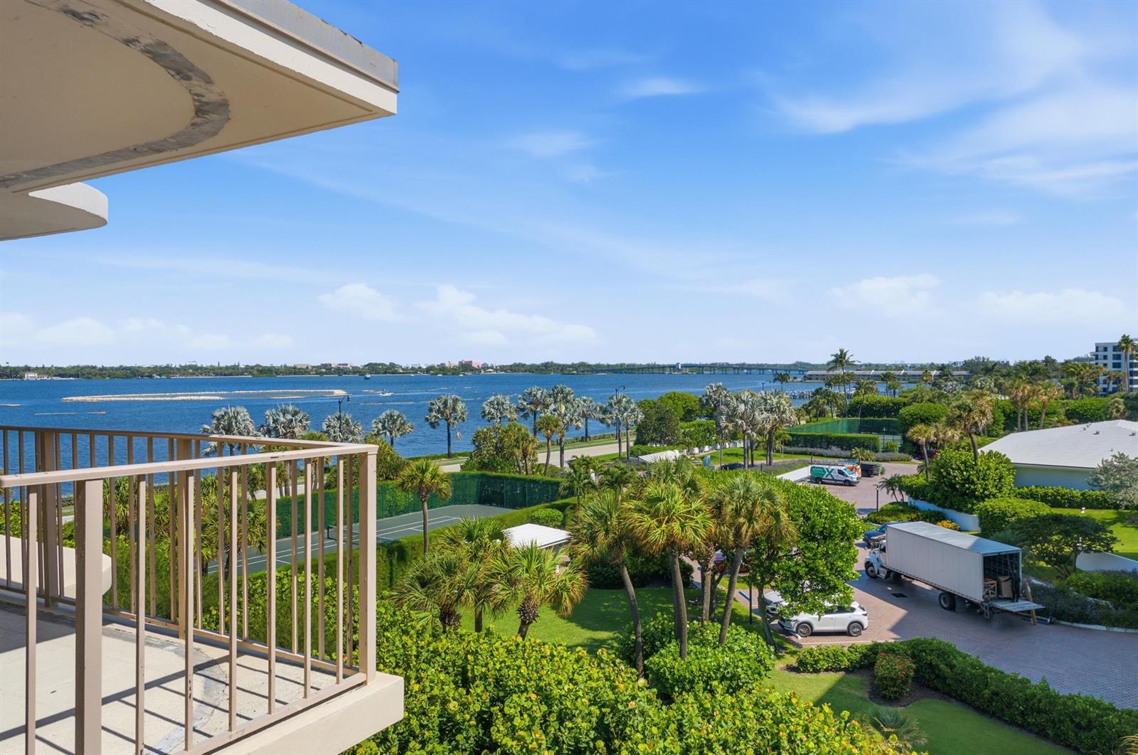 A balcony with a wicker chair and ottoman overlooks a courtyard and a neighboring apartment building — 3200 S Ocean Boulevard # D203, Palm Beach FL 33480, PALM BEACH, FL