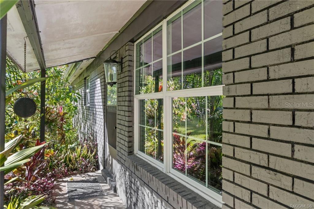 A view of a covered brick porch with a large window and lush garden landscaping — 3751 SE 145TH STREET, SUMMERFIELD, FL