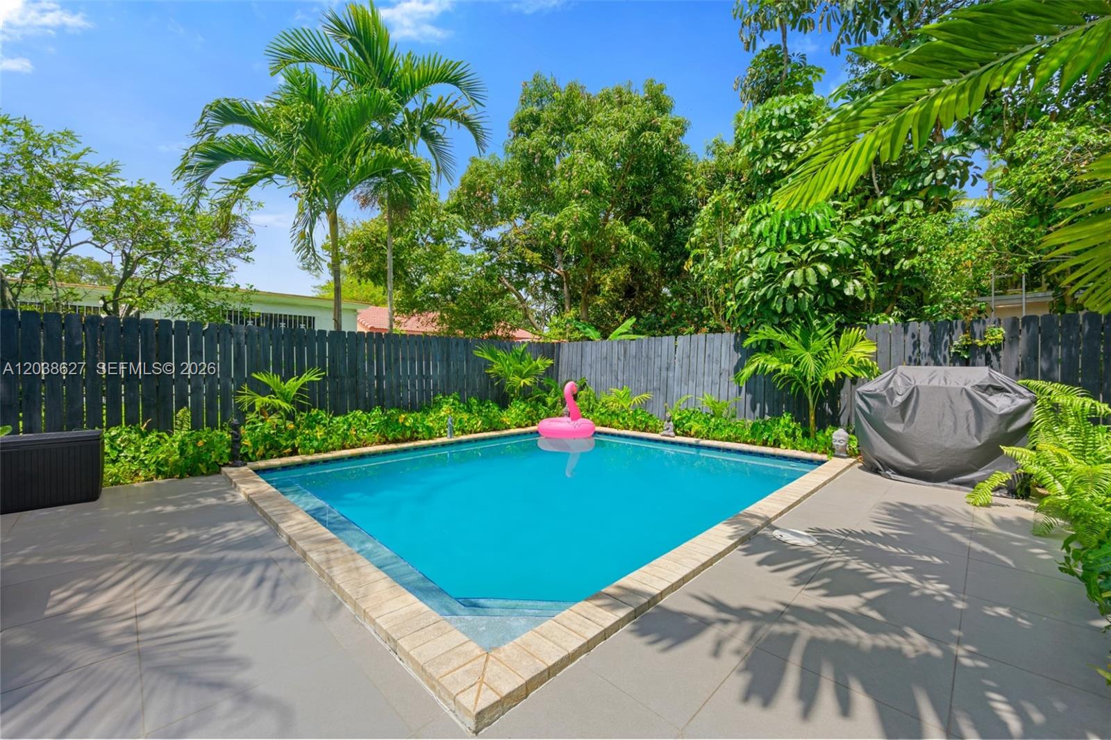 A backyard swimming pool with a pink flamingo float is surrounded by a wooden fence — 761 NE 82nd Ter, Miami FL 33138, MIAMI, FL