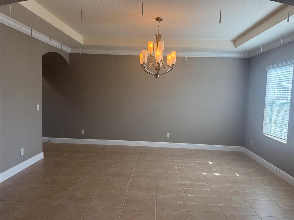 An empty dining room features tile flooring, a tray ceiling with a chandelier, and gray walls — 3128 AMALFI DRIVE, ORLANDO, FL