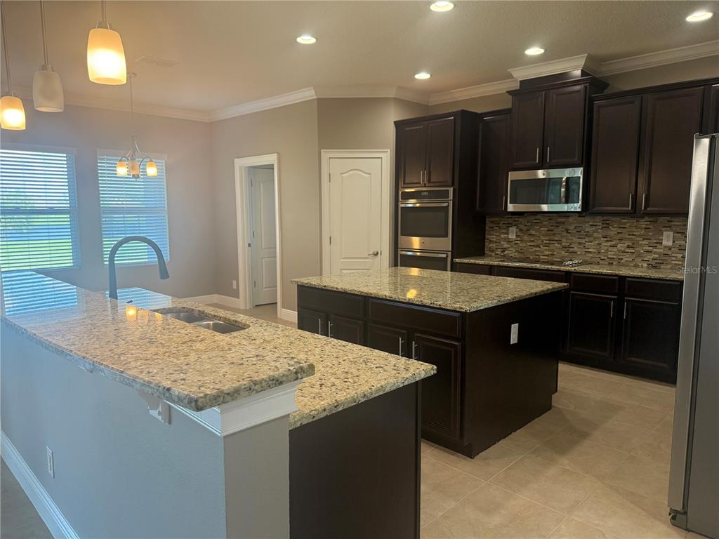 A kitchen features dark wood cabinets, granite countertops, a center island, and stainless steel appliances — 3128 AMALFI DRIVE, ORLANDO, FL